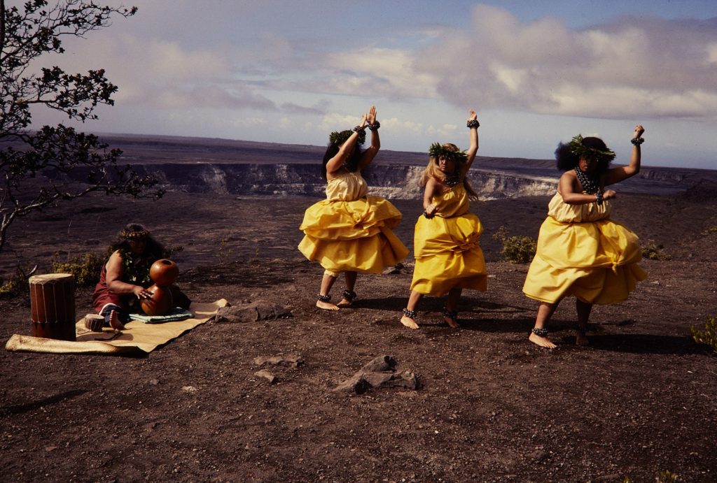 Native Hawaiians performing a dance with a musician playing a Ipu Heke at Hawai'i Volcanoes National Park.