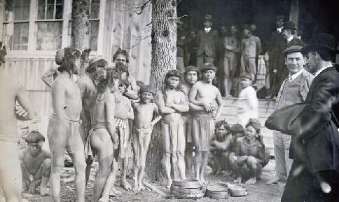 Igorot clad in their native attire pictured with spectating Americans in suits.