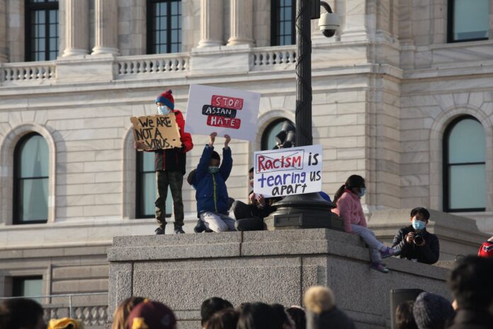 Signs held up by protesters perched on the base of a high statue reads 