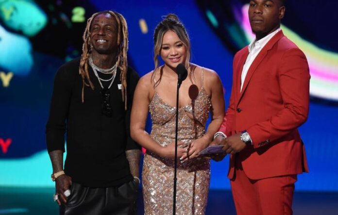 Suni Lee at the ESPYS in 2022 in a sequined dress standing on stage with Lil Wayne and John Boyega