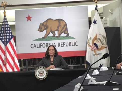 Kamala Harris sits in front of the flag of California speaking to small business owners
