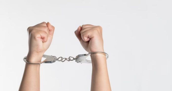 person's wrists in handcuffs as arms are raised in the air