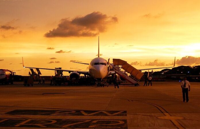 Air India plane sits on runway with an orange glow in the background from a brilliant sunset