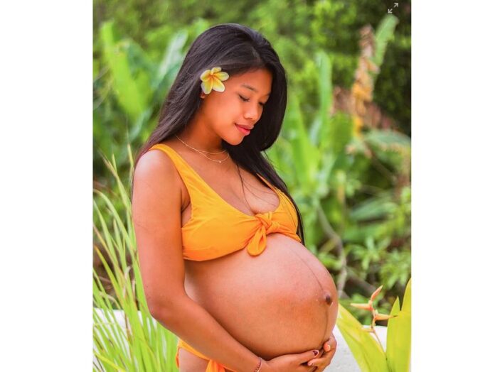 A pregnant Pacific Islander woman holds her belly
