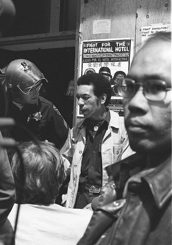 A tenant sympathizer, Calvin Roberts, speaks with a sheriff deputy in an effort to expedite assistance for the evicted tenants. Chris Chow is in the glasses in the foreground . 