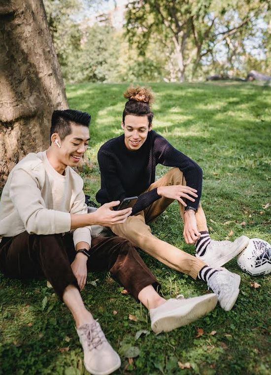 A queer couple shares a moment in the outdoors under a tree