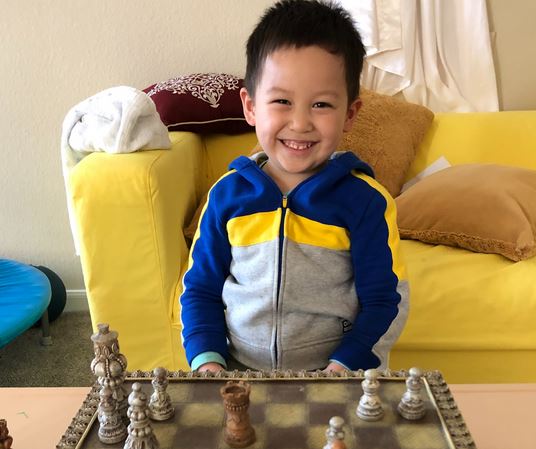 Jeremy flashes a broad grin sitting behind a chess board