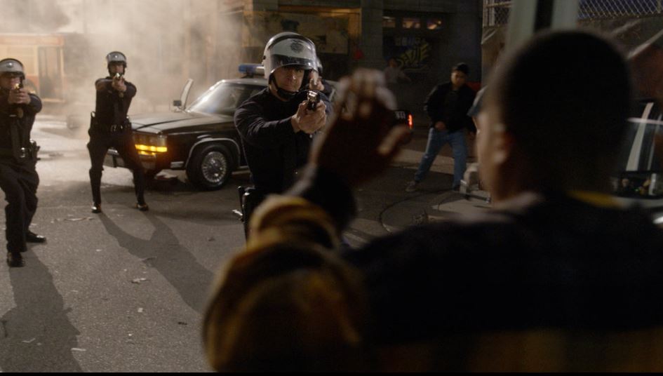 A police officer points a gun directly at a protestor with his hands up on Quantum Leap 