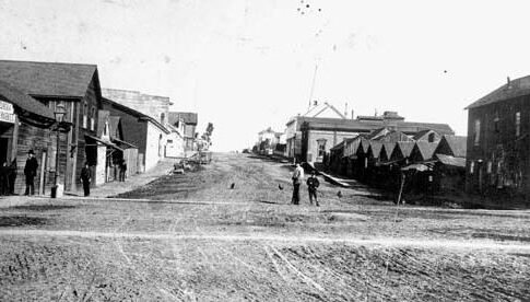 1885 photo of Fourth and E streets in Eureka looking east. Chinatown is on the right and the first few buildings on the left. Eureka City Councilman David Kendall was accidentally shot at this crossing. 中文：1885Eureka。唐人街位于照片右边和左边前几栋房子。David Kendal在这个十字路口被意外射死。