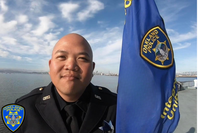 Officer Tuan Le stands next to an Okland Police Department flag
