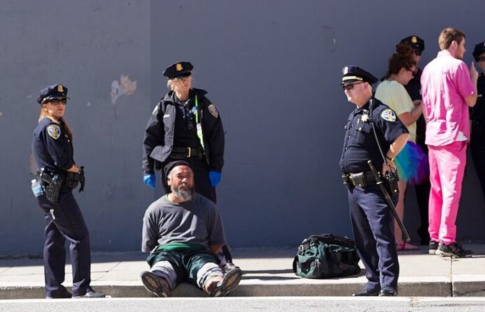 Three San Francisco police officers stand next to man sitting on a sidewalk in San Francisco