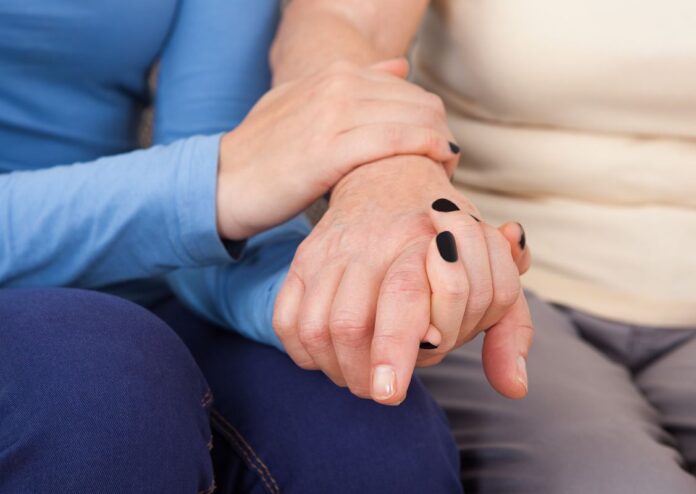 A caregiver places her hand on an elderly woman's hand offering her comfort