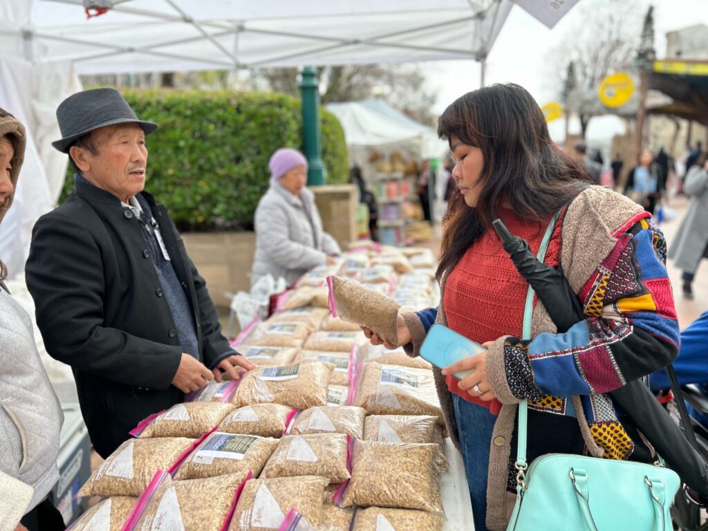 Paj Zeb Vu, left, of Vu Family Farm, speaking with Intha Phomkhai over bags of special new year rice during the Hmong Cultural New Year Celebration. Photo by Jia H. Jung