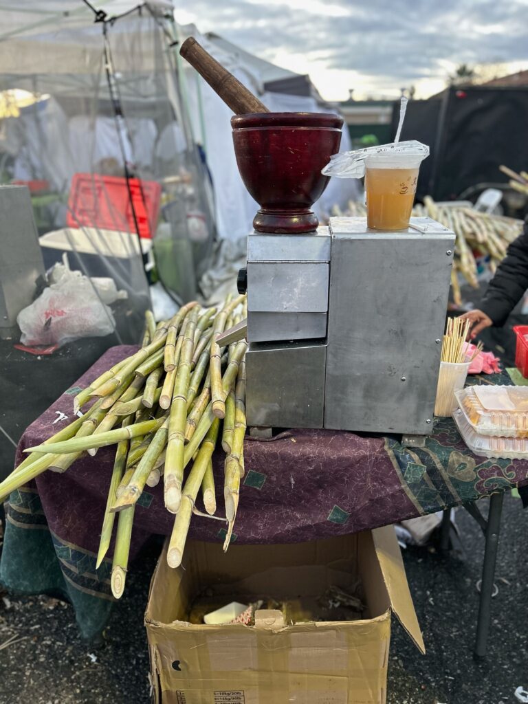 A sugarcane juicing station with a wooden mortar and pestle for mixing papaya salad in the background at the Hmong Cultural New Year Celebration. Photo by Jia H. Jung