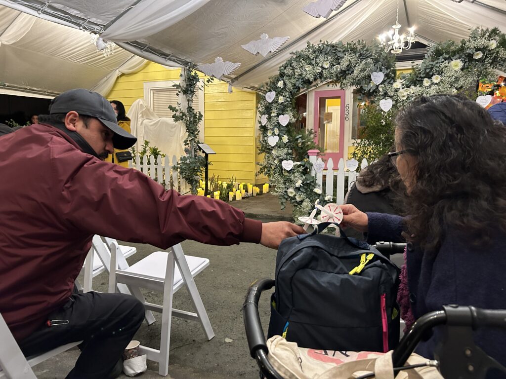 An attendee of the Corazón del Campesino Memorial Evening reached across the aisle to light the candle of Wang Ying Ze (王英则). Mushroom farmers, Half Moon Bay Shooting, Chunli Zhao,Ayudando Latinos a Soñar (ALAS) Casita and Garden at 636 Purissima Street, Jan. 23