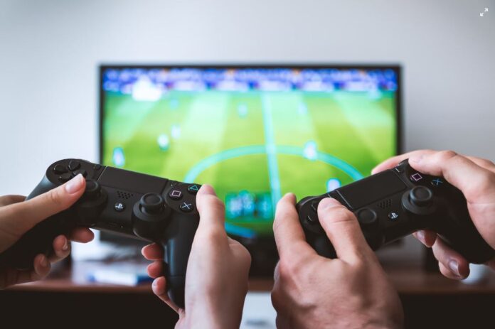 Two pairs of hands work the game remote in front of a large screen TV