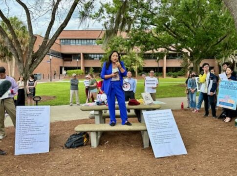 a protester stands on a table at the University of Florida deploring a law that bans cooperation between the University and people from China and six other nations.