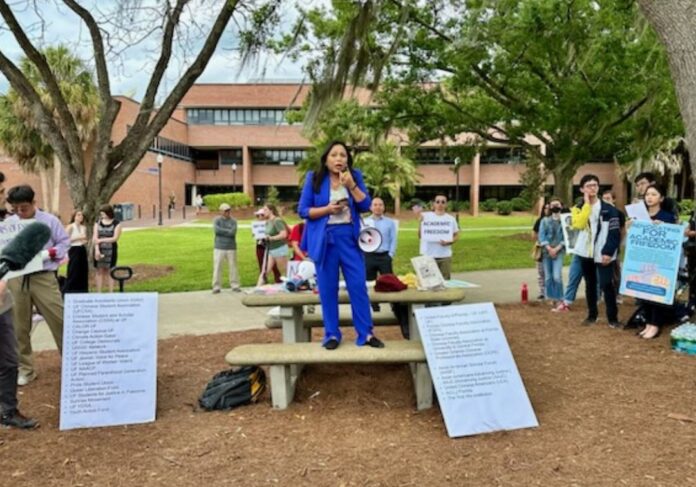 a protester stands on a table at the University of Florida deploring a law that bans cooperation between the University and people from China and six other nations.