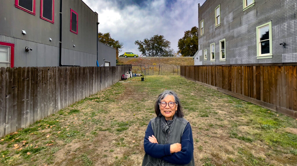Woman stands in front of vacant lot.