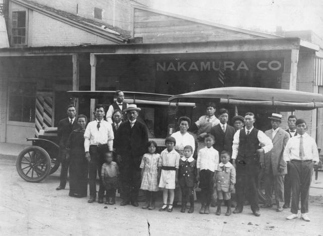 A group of children and adults stand in front of two delivery trucks.