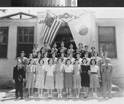 A group of high school students and their teachers pose in front of American and Japanese flags.