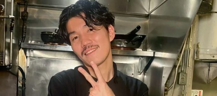 Wataru Kakiuch puts up the victory sign in this photo inside a kitchen