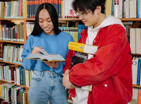 Two Asian American students going through a book together at a library