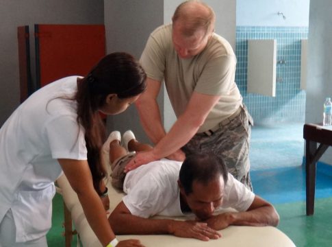 A Filipino nurse assists a doctor examining a patient on a medical table