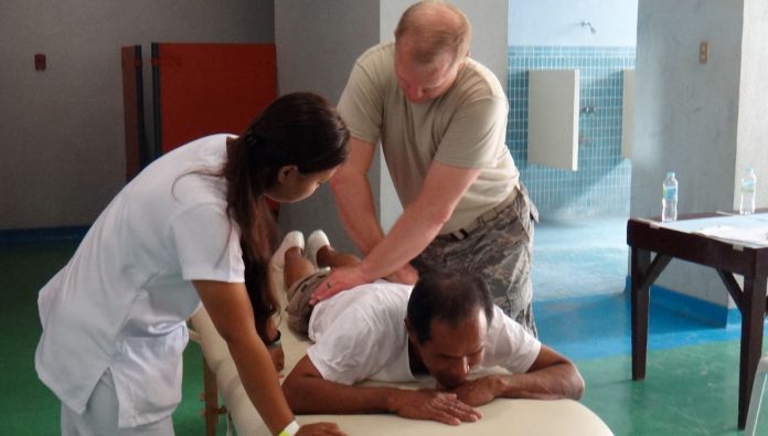 A Filipino nurse assists a doctor examining a patient on a medical table