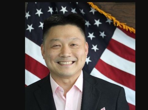 Yu-Ching James Pai smiles in front of an American flag