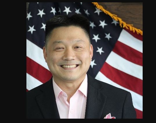 Yu-Ching James Pai smiles in front of an American flag