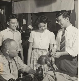 From the WRA: “Here are a group of Japanese Americans who are employed at the Y.M.C.A.
Tailor Shop as part-time and full-time workers. Reading from left to right are Edward Koyama from the
Rohwer Relocation Center, who is working part-time while attending the St. Louis School of Pharmacy;
Susie Tamaki, also a part-time worker, came to St. Louis from the Tule Lake Relocation Center and was a
former resident of Tacoma, Washington; Frank Hayashi who manages the tailor shop formerly resided in
Berkeley, California, and relocated from the Jerome Relocation Center approximately a year and a half
ago. In the foreground is Mr. Frank Wiltpert, a good humored tailor. Photographer: Iwasaki, Hikaru St.
Louis, Missouri.”
Courtesy: WRA Photo, UC Berkeley, Bancroft Library