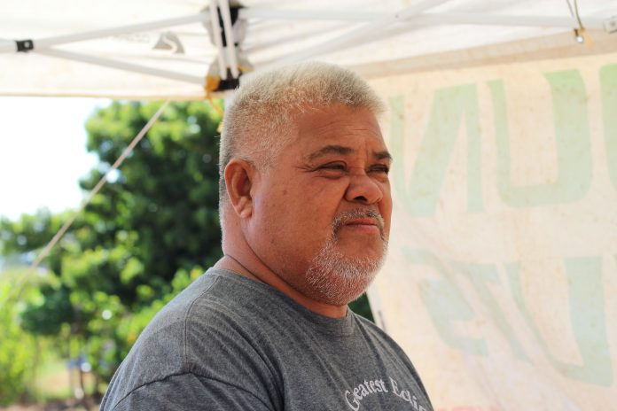 A portrait of a Koli Hafoka. He has close-cropped gray hair and a beard. He's wearing a blue t-shirt.