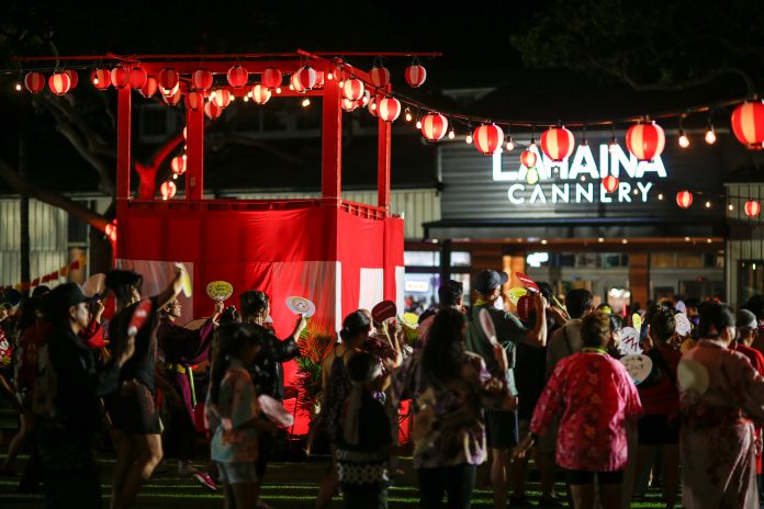 Hundreds of participants gather around a drum tower with red lanterns at night time.