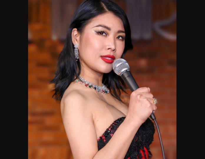 Comedienne Jiaoying Summers stands sideways holding a microphone