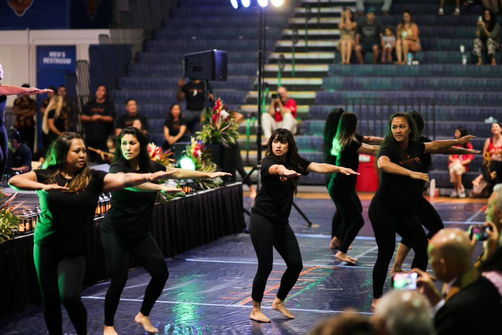 A line of women dressed in black t-shirts and black leggings dance together.