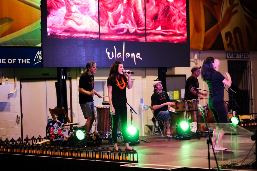 A singer stands on stage with drummers behind her.