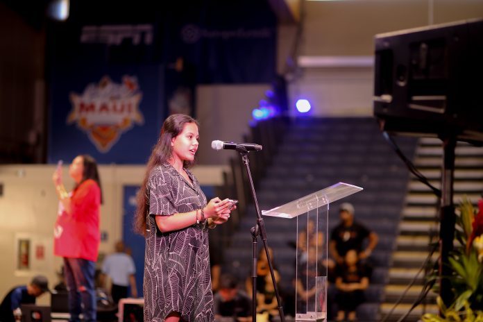 Seventeen-year-old Kawekiu Palakiko speaks in front of a gymnasium auditorium about surviving and rebuilding after Lahaina's wildfire.