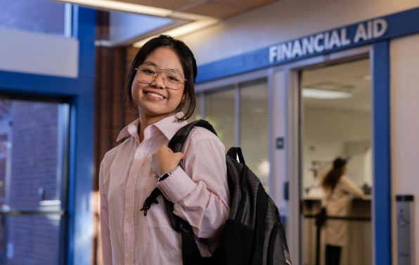 Student with a backpack poses in front of financial aid office