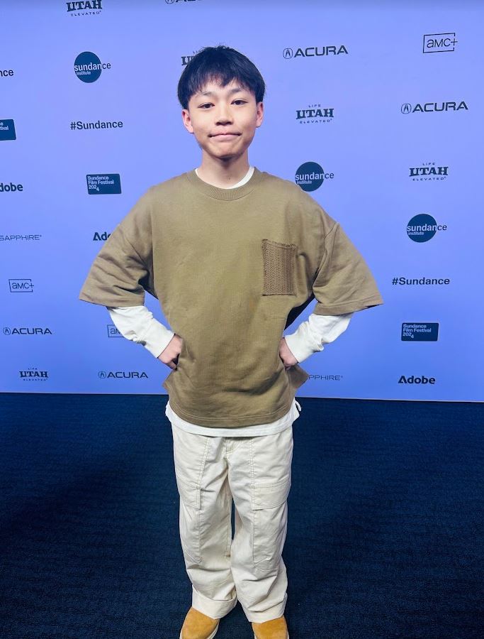 Izaac Wang poses in front of the step and repeat at Sundance 