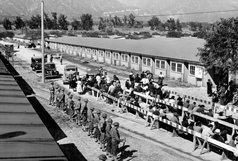 The evacuation of Japanese-Americans from West Coast areas under U.S. Army war emergency order. Japanese waiting for registration at the Santa Anita reception center. Photograph shows Japanese-Americans in lines next to horse stalls as armed guards observe.