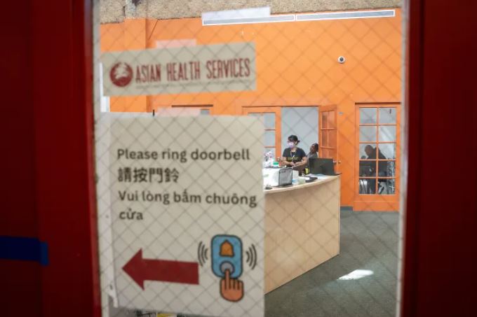 Doorway at Asian Health Services with community workers seen through the glass panel. 