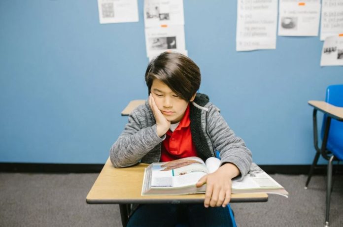 Boy sits alone at his desk looking depressed and lonely