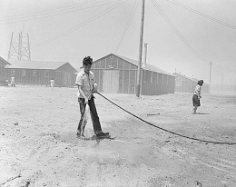 Young man squirting water on dusty road.