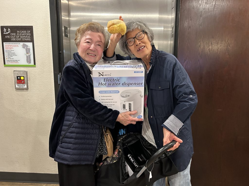 82-year-old Jones Senior Homes evacuee Oh Kyeong, left, and the daughter of a 99-year-old resident, right, pose with in-kind donations from community workers