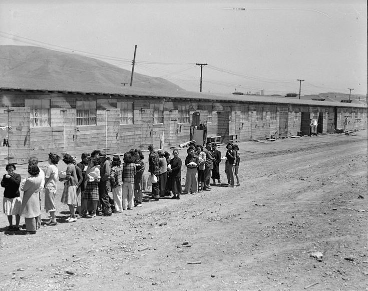 Families, mostly women, stand in line outside what appears to be barracks at the Tanforan Detention Center in San Bruno, CA 