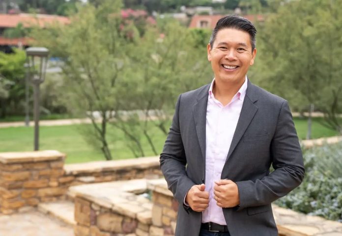 Derek Tran poses in a garden with his hands tugging on his sports coat