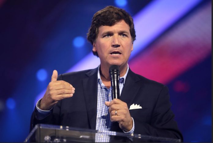 Tucker Carlson with a microphone in one hand and gesturing with the other