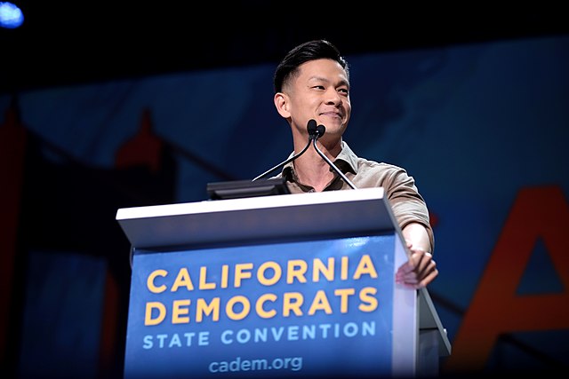 A photo of Evan Low standing at a podium that says 