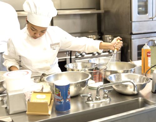 A culinary student participating in an apprenticeship program cooks in the kitchen of a restaurant.